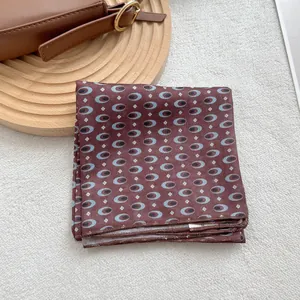 Detail view of a folded dark brown square scarf with geometric eye patterns on a wooden stand