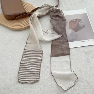 Detail of thin linen scarf with brown and cream stripes styled on a leather bag