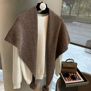 Close-up of brown heavy knit wool triangle shawl with decorative pom-poms on the edge