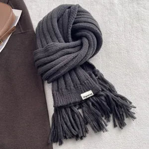 Close-up of charcoal grey knit scarf with long tassels and branding label detail
