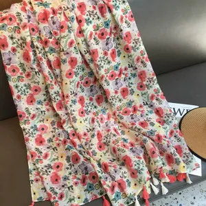 Detail view of summer floral scarf with red tassels and blue flower print on grey sofa