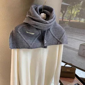 Close-up of gray knitted button scarf with diamond weave pattern and brand label