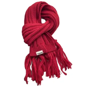 Thick red knit scarf with fringe tassels and brand label on a white background