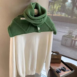 Detail shot of the green knit scarf with diamond texture and white button fastener