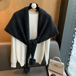 Textura detallada de bufanda triangular de lana gris oscuro con pompones en una percha