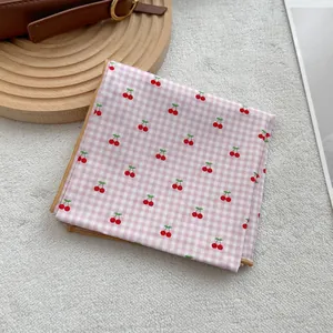 Pink checkered cherry print silk scarf with yellow stitched edges on soft background