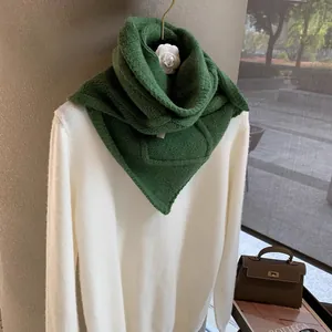 Detail of green knit triangular scarf paired with white sweater and stylish accessories