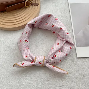 Detailed view of pink plaid cherry print scarf tied in a bow on textured rug