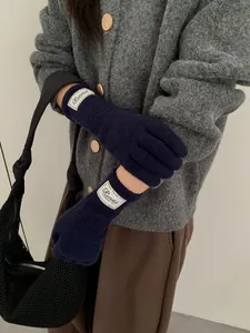 Detailed knit texture and logo patch on dark blue winter gloves worn by a person