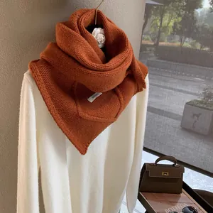 Close-up of burnt orange knit scarf texture with brand tag on white sweater