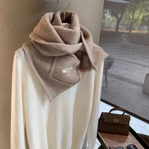 Detailed close-up of thick beige chunky knit scarf with premium brand woven label