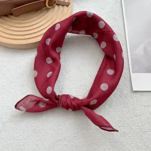 Gros plan d'un foulard en soie rouge à pois ondulés blancs sur un plateau en bois décor