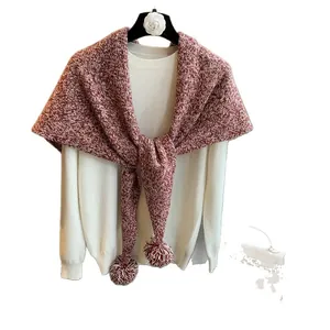 Elegante chal de lana tejida burdeos y blanco con pompones sobre un suéter blanco