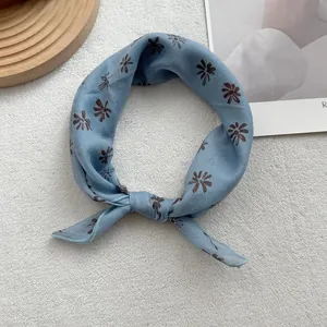 Close-up of knotted misty blue floral cotton linen scarf on a minimalist textured background