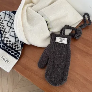 Détail de moufles en tricot gris foncé et écharpe crème à motifs géométriques sur bois