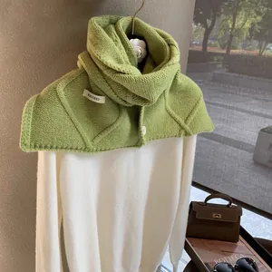 Detail of green knitted wool scarf with white buttons and brand tag on white sweater