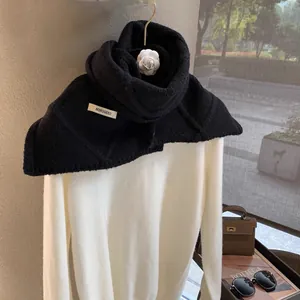 Detail of black wool knit shawl with white camellia pin and brand label on a white sweater