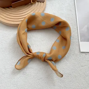 Gros plan d'un foulard en soie jaune noué à pois bleu clair sur un plateau en bois
