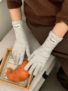 Detail view of light grey knitted gloves with brand logo label and soft wool texture
