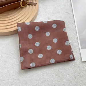Détail d'un foulard carré marron à pois avec texture lisse et bords aux finitions soignées