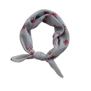 Light blue cotton linen square scarf with red daisy pattern knotted on white background