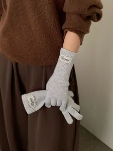 Detail of light grey knitted winter gloves featuring a white woven label on the wrist cuff