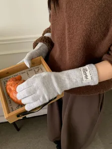 Detail of light gray knitted gloves with custom textile label on warm sweater background