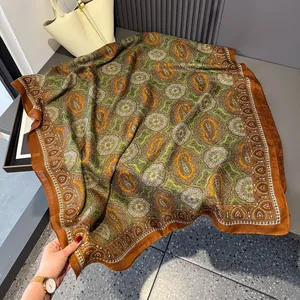 Detail of vintage paisley silk scarf styled with a luxury handbag on a grey surface