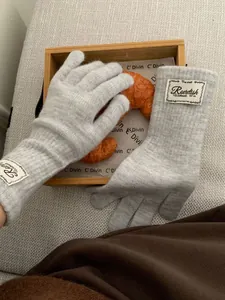 Detail of light gray knitted gloves with woven label on soft wood and fabric background