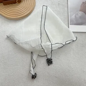 Detailed view of a white lace triangle scarf with grey wavy edges and pompom tassel charms