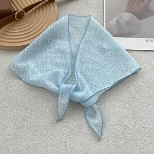 Detail view of light blue lace triangle scarf with floral patterns on a texture background