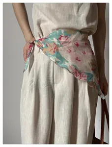 Close-up of floral chiffon scarf tied at the waist over beige linen trousers