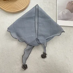 Close-up of gray sheer triangle headscarf with dark pom-pom tassels