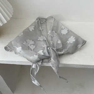 Detail van grijze driehoekige sjaal met witte ginkgo-bladpatronen en transparante stof