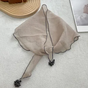 Close-up of light brown lace scarf with wave edges and grey tassel details on fabric