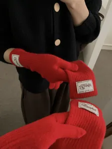 Detail view of red knitted gloves featuring ribbed cuffs and white woven label