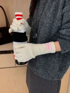 Detail of cream white knit gloves featuring a pink square brand tag on the ribbed wrist