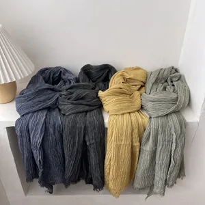 Solid color pleated scarves in multiple tones with fringe edges on stone surface