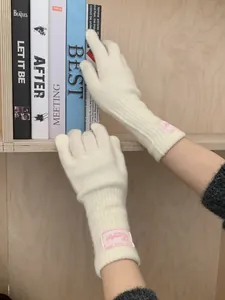 Detail of cream knit arm warmers featuring a pink woven label and soft wool texture