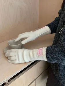 Close-up of white knit gloves with ribbed cuffs and a pink brand label detail