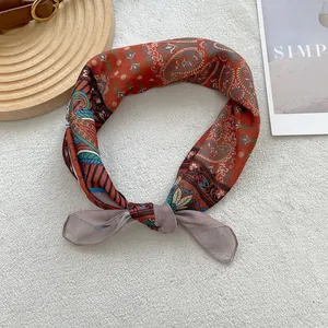 Detail of rust red paisley cotton linen scarf tied in a knot on a soft white texture