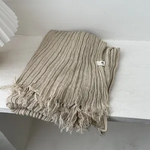 Detail shot of beige pleated cotton scarf with raw fringe edges and soft texture fabric