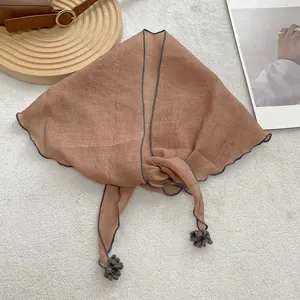 Detail of reddish-brown triangle scarf with wavy edges and small grey pompom tassels