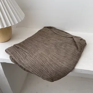 Detail of dark brown pleated scarf with fine vertical texture on white table background