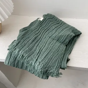 Detail of sage green pleated cotton linen scarf with frayed edges on white wood