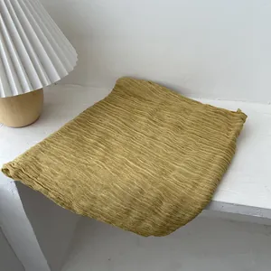Detail of mustard yellow pleated scarf with textured fabric on a white wooden step