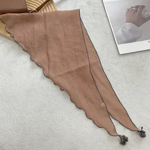 Close-up of terracotta lace triangle scarf with wavy edges and mini pom-pom details