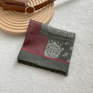 Dettaglio di un foulard quadrato con motivo paisley verde scuro e bordo a quadri