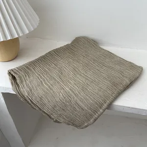 Close-up of light khaki pleated scarf with soft texture draped on a white shelf