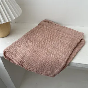 Detail of soft linen scarf in dusty pink folded neatly on a wooden desk with table lamp